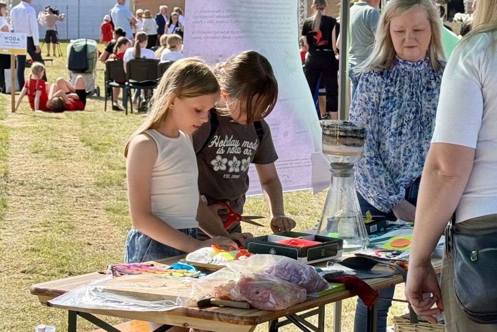 Dzieci przy stoisku edukacyjnym przeprowadzają eksperymenty z naukowcami.